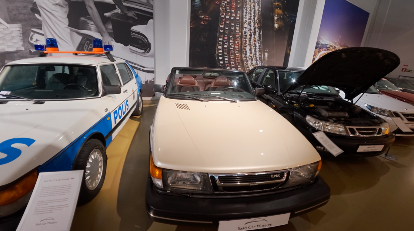 Saab 900 Turbo Tre bilar i en utställning, inklusive en vit cabriolet och några andra modeller.