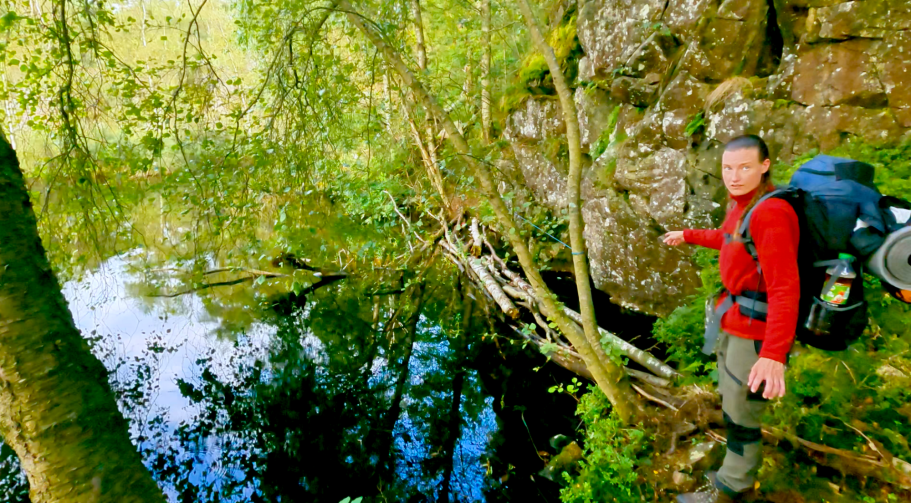 2:a vattenhindret Vandrare vid en sjö med ryggsäck, omgiven av grönska och klippiga kanter.