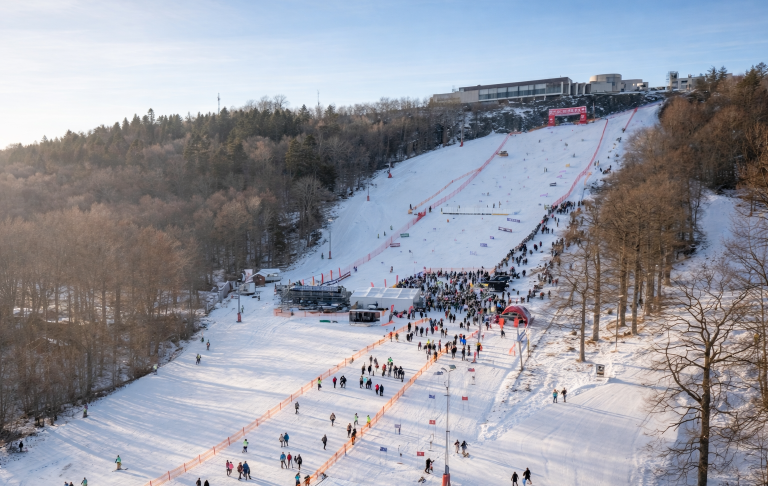 Vinterlandskap med skidbacke och människor som åker skidor. Klara himmel och snöigt område.