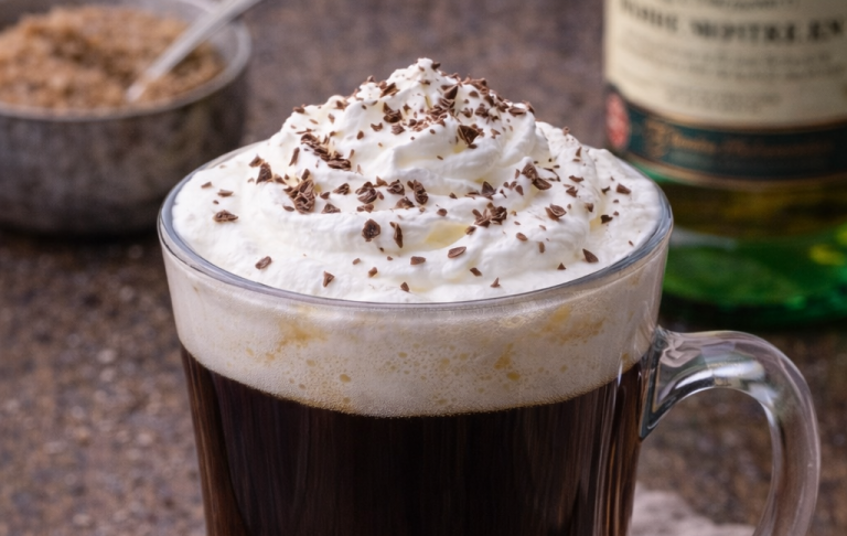 Kopp med kaffe, vispad grädde och chokladströssel, med socker i bakgrunden.