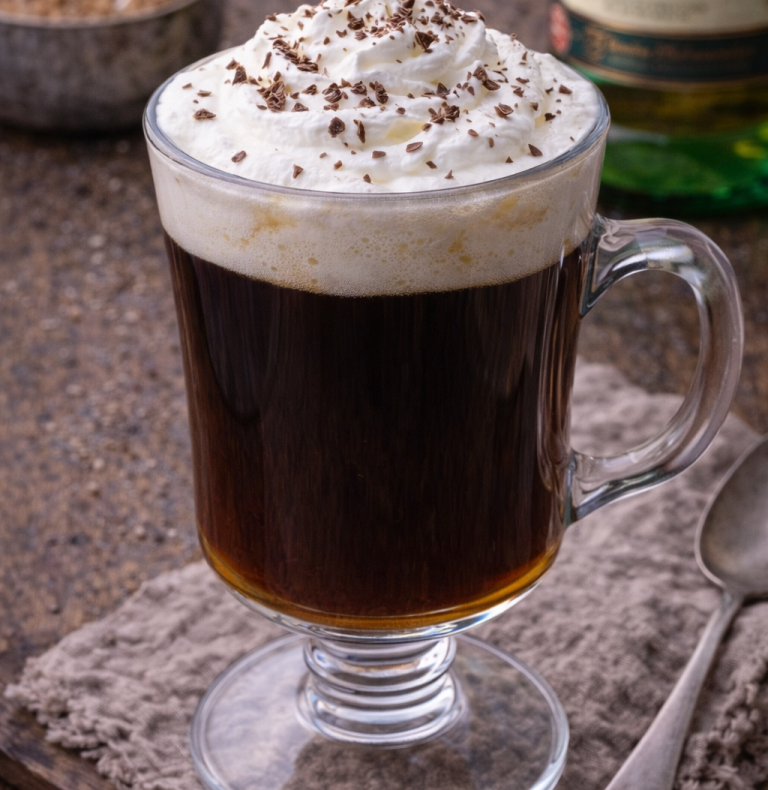 En glas kopp med kaffe, toppad med grädde och chokladspån.