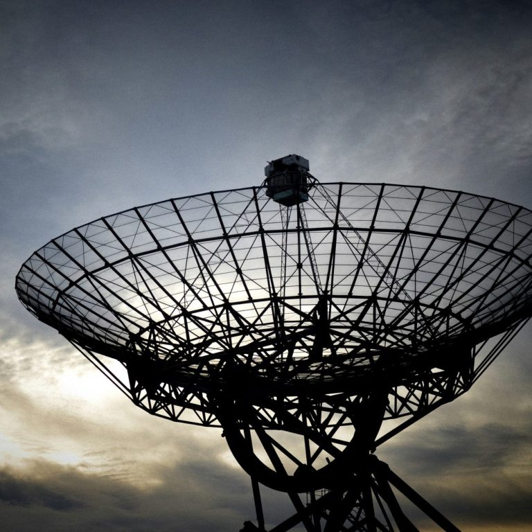 Stor paraboliskt antenn med silhuett mot en grådaskig himmel.