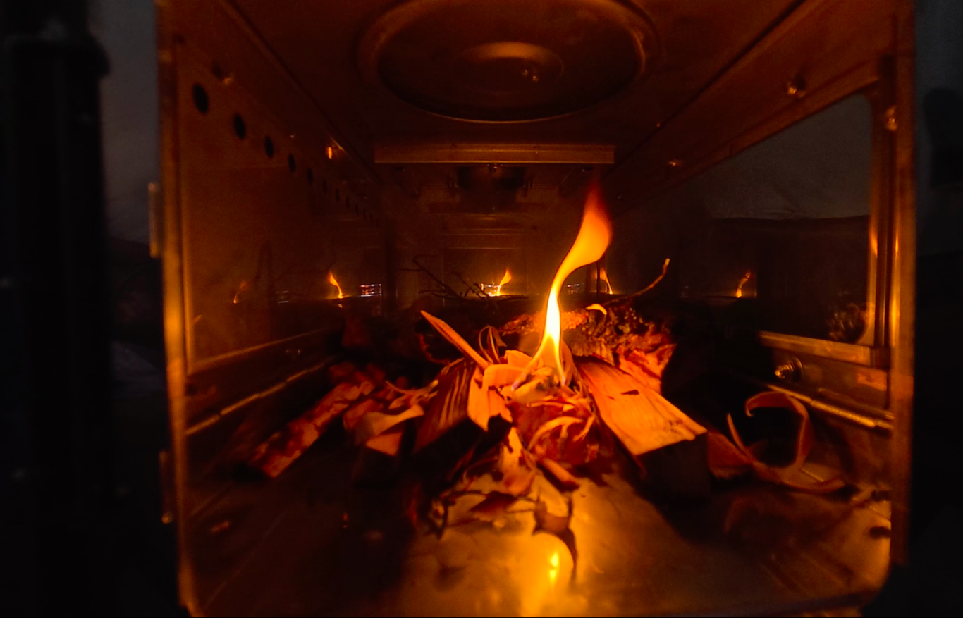 Tänder kaminen Eldslåga på brännbart material i en ugn, omgiven av skugga.
