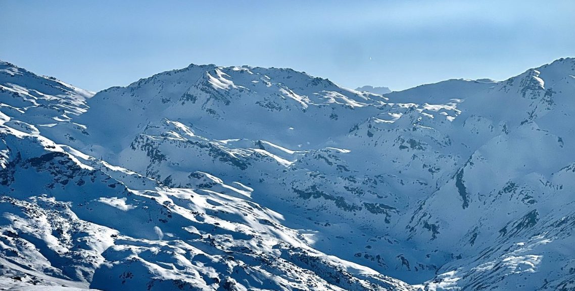 Snötäckta alpberg med klippor i olika nyanser av blått och vitt under en klar himmel.