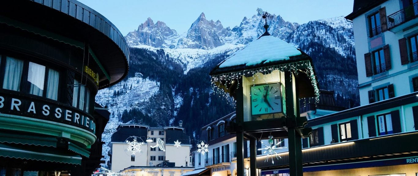 Utsikt över snöklädda alpberg och en gammaldags klocka i en alpstadsmiljö.