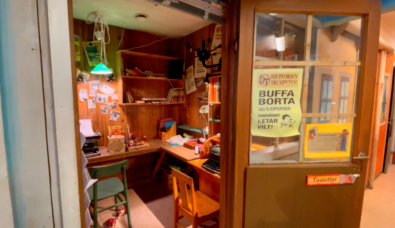 Postkontoret Ett rum med skrivbord, stolar och väggar prydda med bilder och affischer.