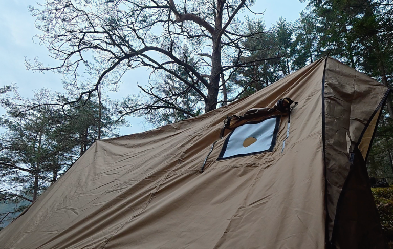 Tält med ett fönster, omgiven av träd i en dimmig skogsmiljö.