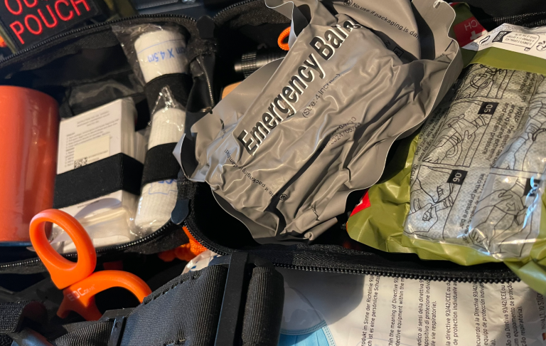 Öppnad väska med nödutrustning, inklusive första hjälpen och försörjningsartiklar.