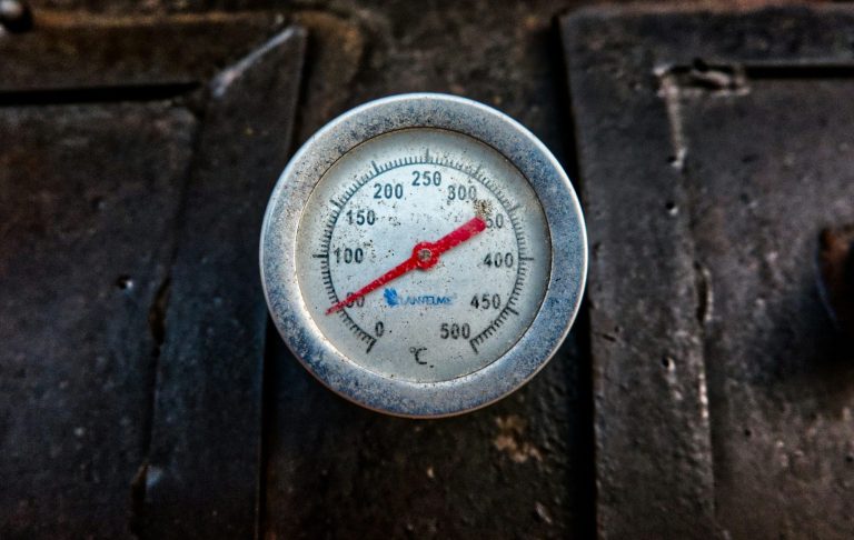 Termometer med röd nål som visar temperaturen på en svart yta.