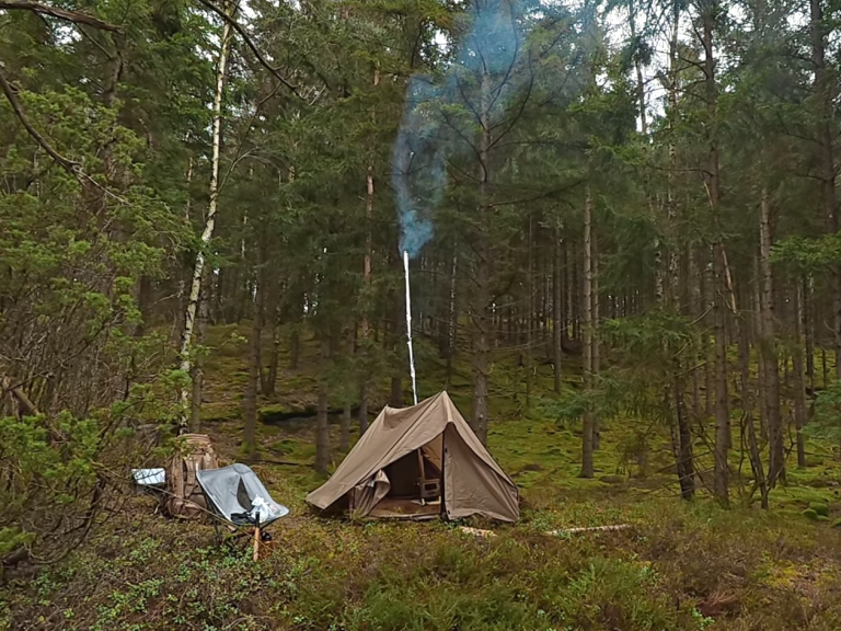Tält i skogen med rök som stiger från en skorsten, omgiven av träd.