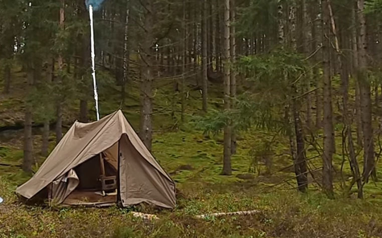Ett hot tent i en skog med träd och mossig mark runt omkring.
