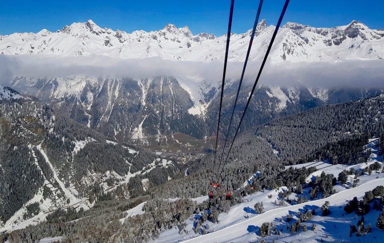 Berglandskap med snötäckta toppar och en kabinbana som svävar över dalen.