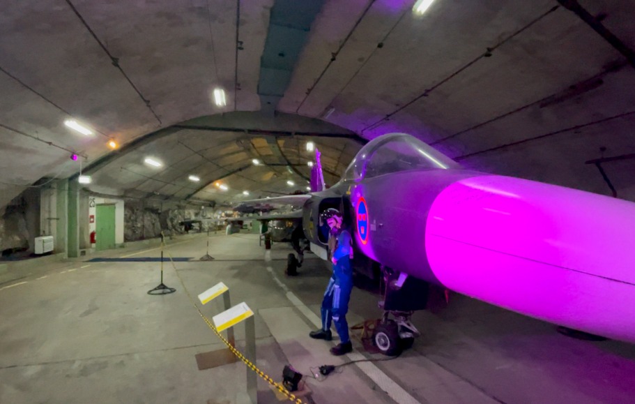 Pilot och jetflygplanet JAS39Gripen inuti en Bunker-hangar med lila belysning.