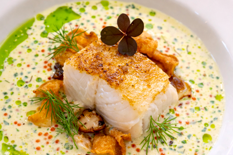 Stekt fiskfilé med kantareller och gräddsås, dekorerad med örter och färgglada prickar.