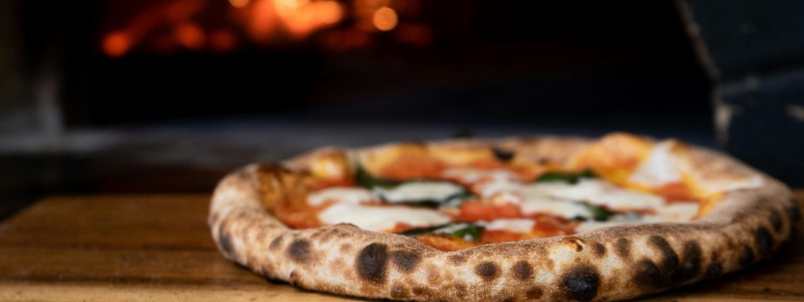 Nygräddad pizza med tomatsås, mozzarella och färska basilika på ett skärbräde.