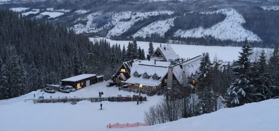Stort hus i snön med svaga ljus och omgiven av fjäll och skog.