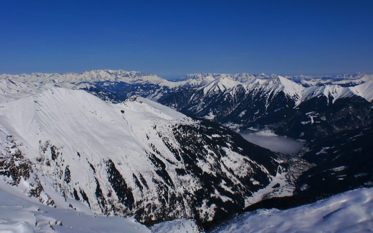 Snöklädda berg med klara blå himmel och dalar i fjärran.