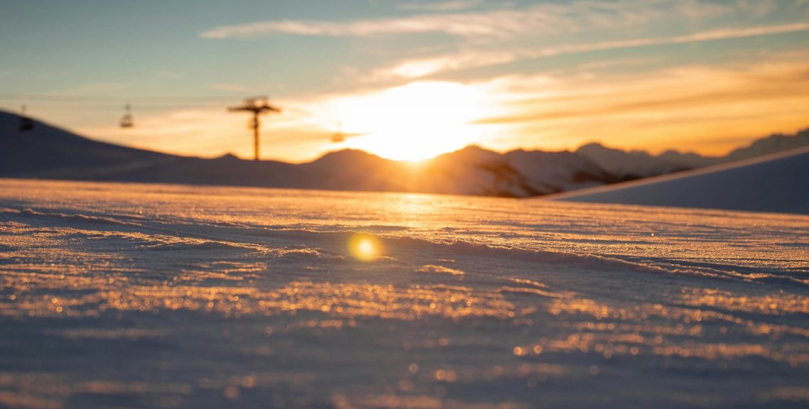 Solen går ner över snötäckta fjäll med en skidlift i bakgrunden.