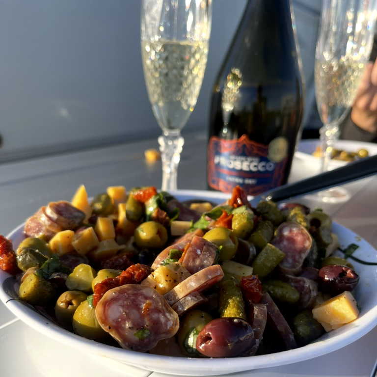 En tallrik med grönsallad, charkuterier och ett par glas champagne i bakgrunden.