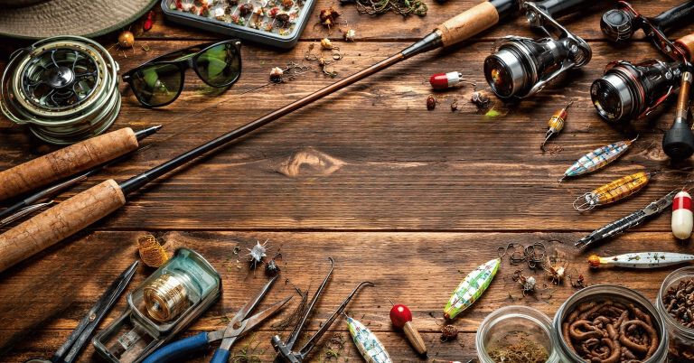 Fiskeutrustning och verktyg på ett träbord med detaljer som beten och spön.