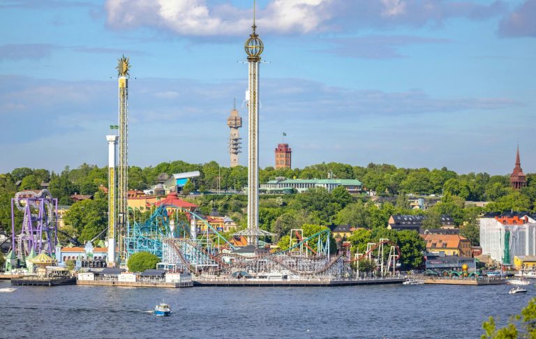 Färgglad nöjespark vid vattnet med berg-och-dalbanor och torn.