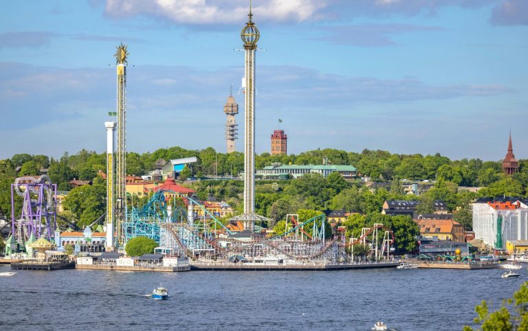 Nöjespark vid en sjö med nöjesåkturer och gröna omgivningar.