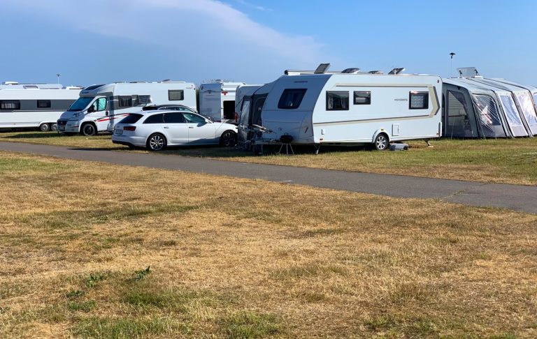 Campingsplats med flera campingvagnar och en bil på gräsmatta under blå himmel.