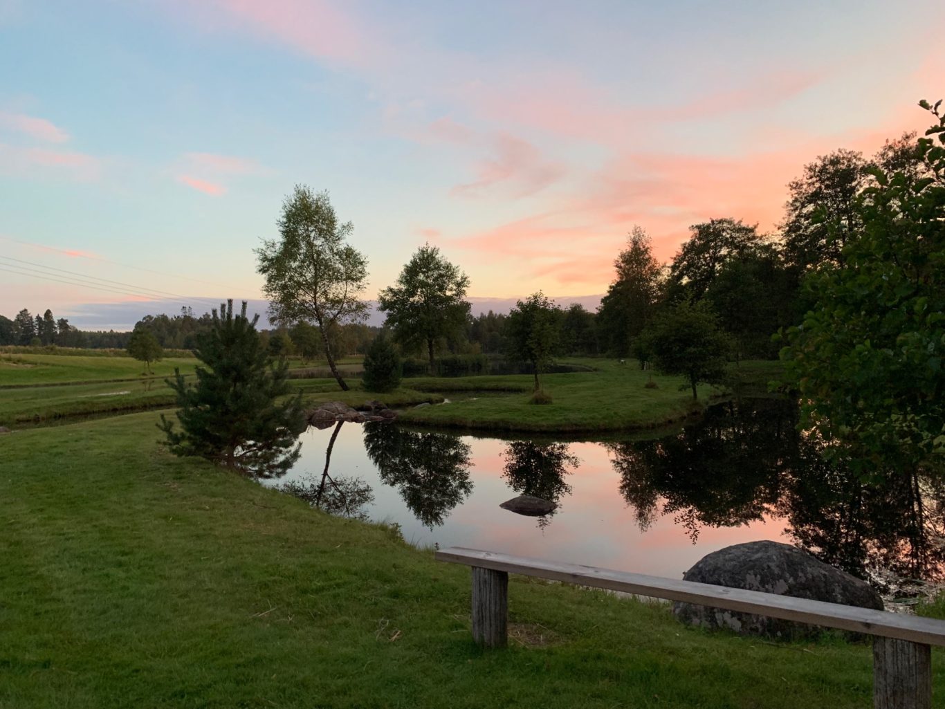 Kvällssol i Flugströmmen hos Sunnedamm Lugn sjö med gröna omgivningar och rosa himmel vid skymning.