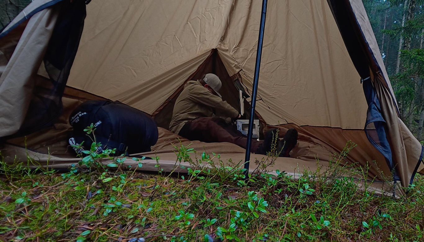 Monterar skorstenen Två personer sitter i ett tält, en ligger på marken och en annan arbetar.