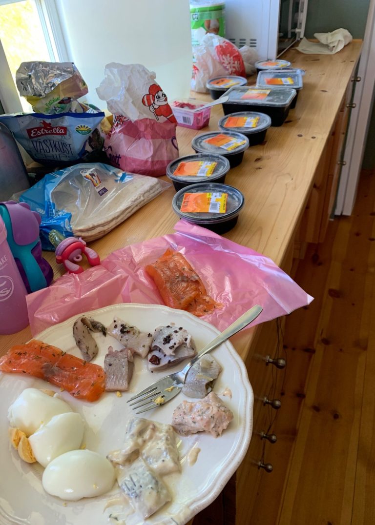 Tallrik med rester av mat och flera behållare med förpackad mat på en bänk.