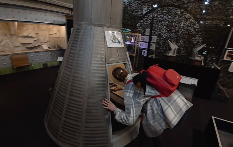 Rymdkapsel på Aeroseum Besökare i en utställning, lutar sig fram mot en interaktiv installation.