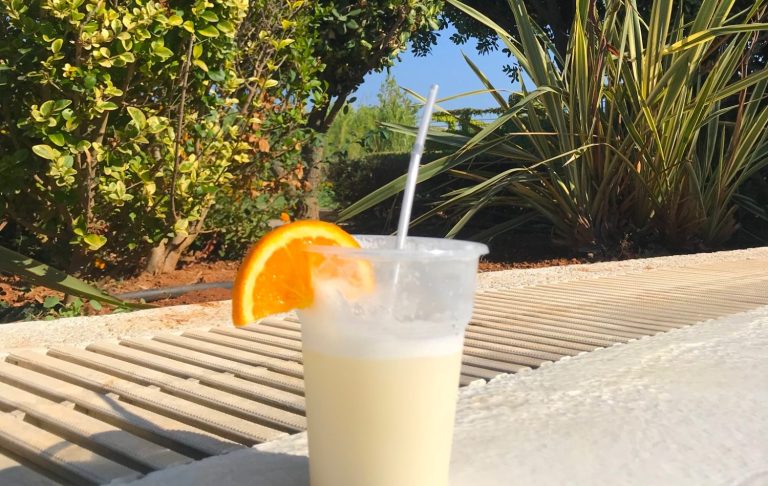 En plastmugg med vit drink och en skiva apelsin, placerad på en grå yta.