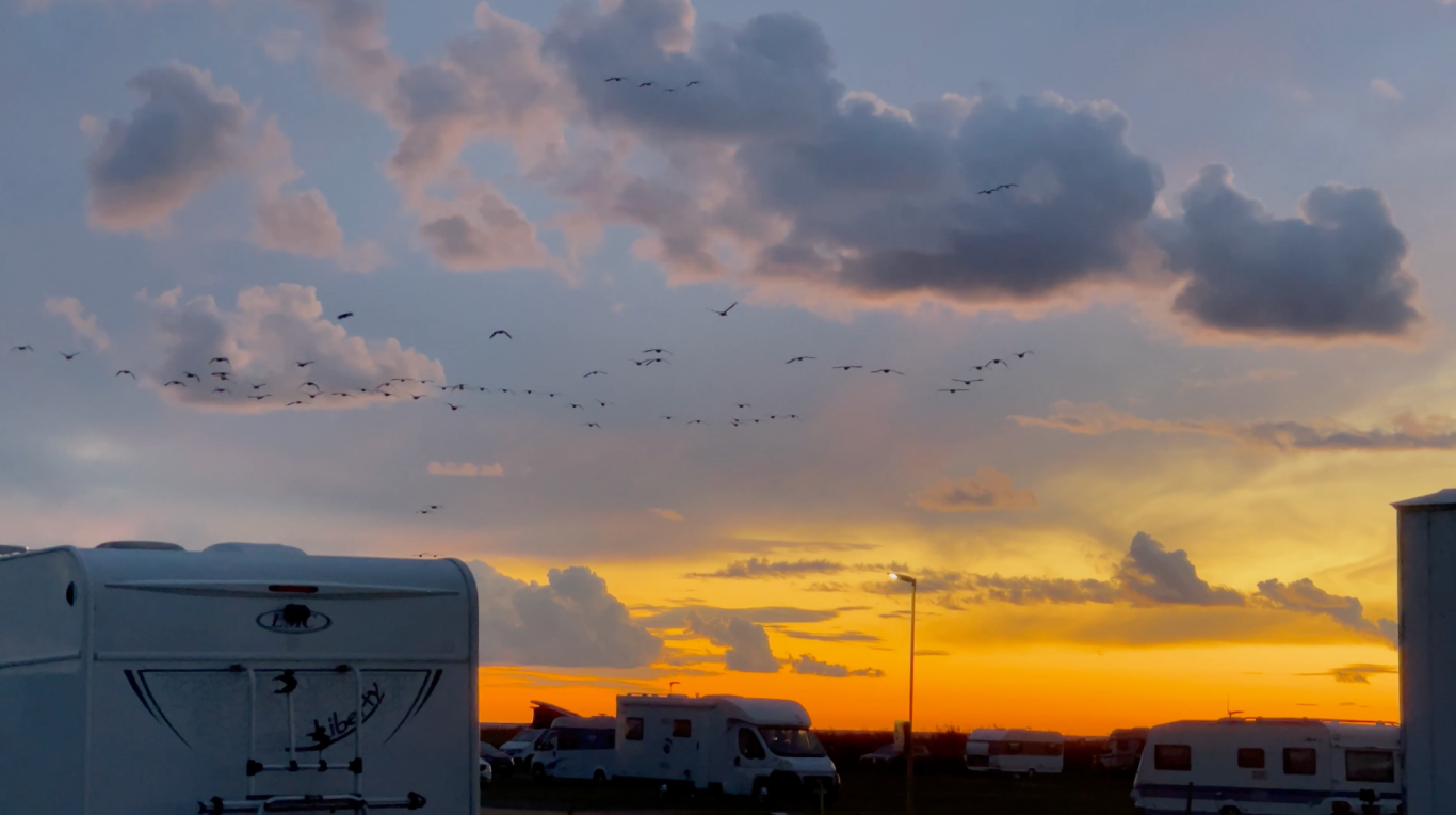 Solnedgång sommarkväll på Björkängs Camping Solnedgång med färgglada moln över husvagnar på en campingplats.
