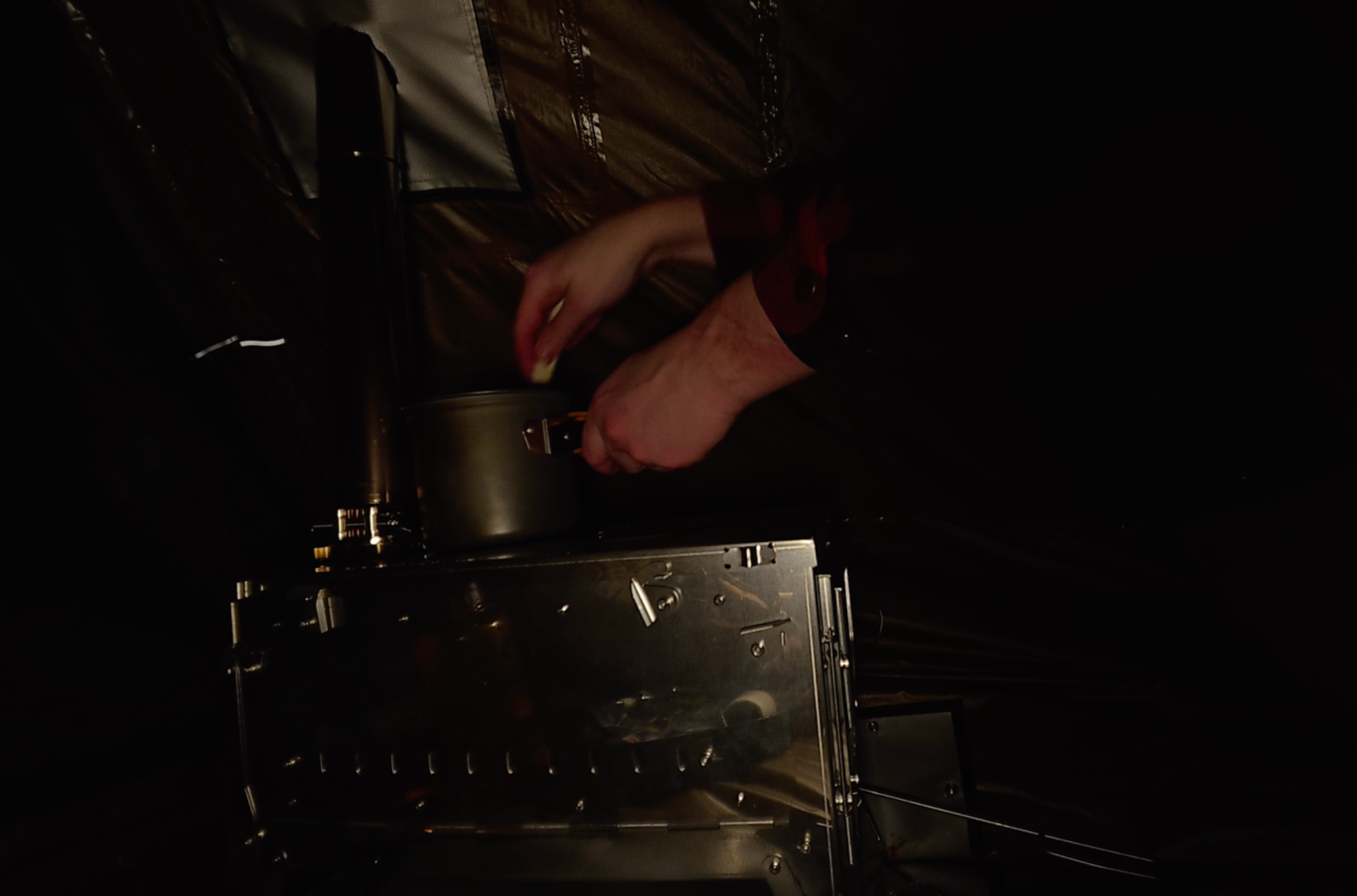 Lagar köttgryta på kaminen Händer som justerar en metallbehållare i svagt ljus.