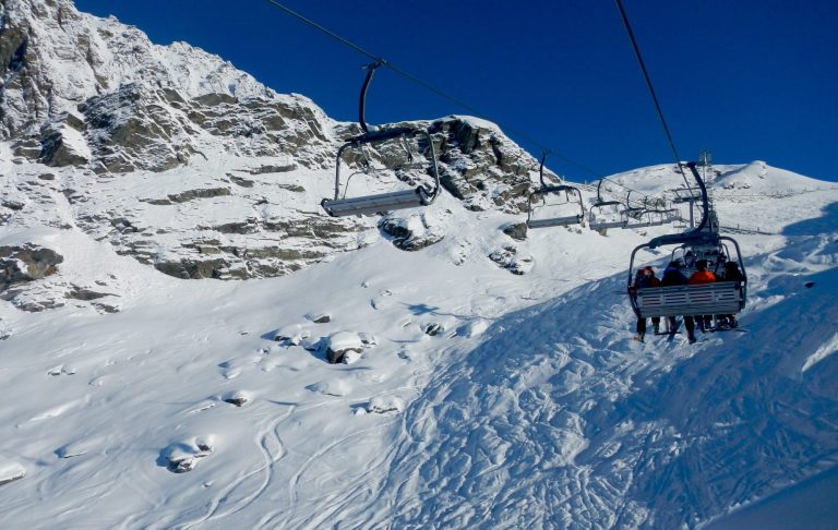 Ski lift över snötäckta fjäll och berghang under klarblå himmel.