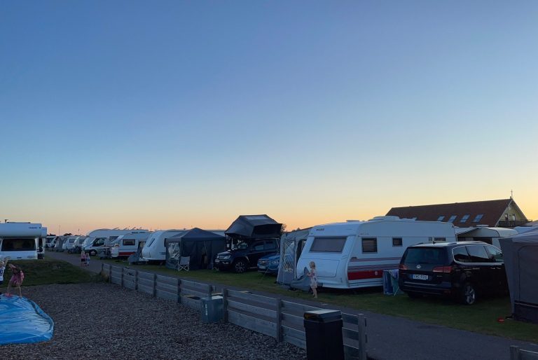 Solnedgång på Skrea Camping Campingtält och husvagnar radade längs en grön gräsmatta under en klar himmel.