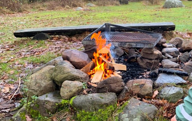 Eld brinner i en stenlagd lägereld med grön gräsmatta runtom.