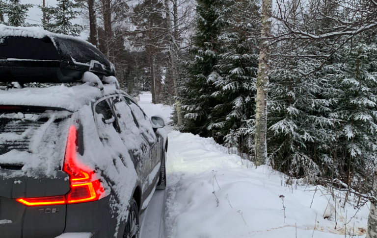 Snöig bil en vinterdag En bil parkerad vid en snötäckt väg i en skog med granar.