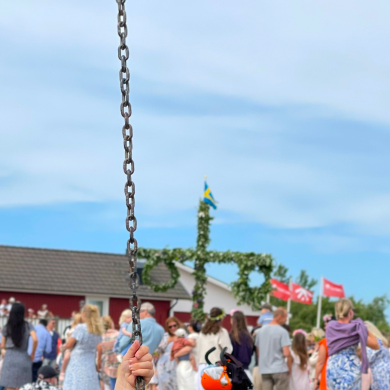 Midsommarfirande med en majstång och människor i festkläder.