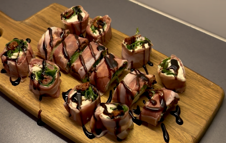 Sushi med olika fyllningar, inlindade i bacon och toppade med sås på en träskärbräda.