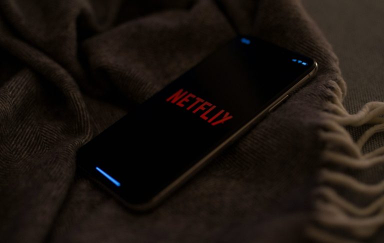 En smartphone med Netflix-logotyp på en mörk filt.