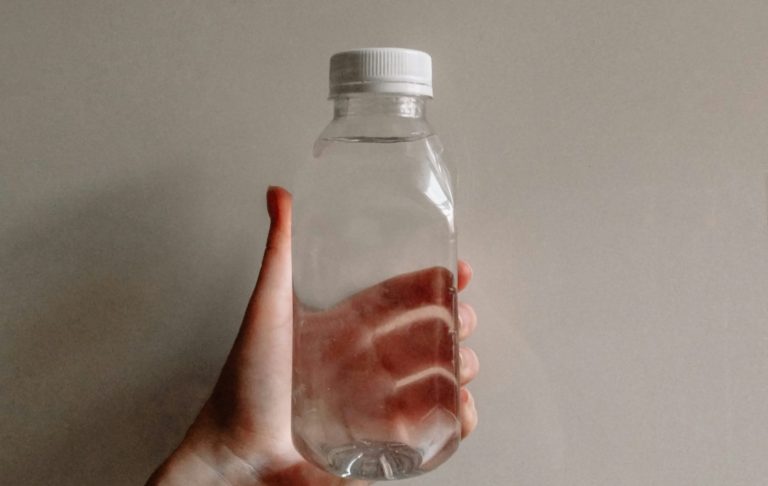 En hand håller en genomskinlig plastflaska med vit kork.