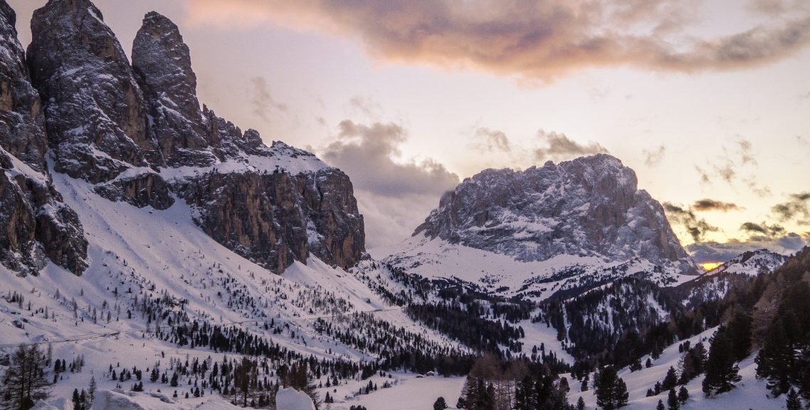 Snöklädda bergstoppar under en pastellfärgad himmel vid solnedgång.