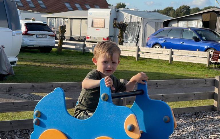 Ett barn leker på en blå leksaksdino på en lekplats vid camping.