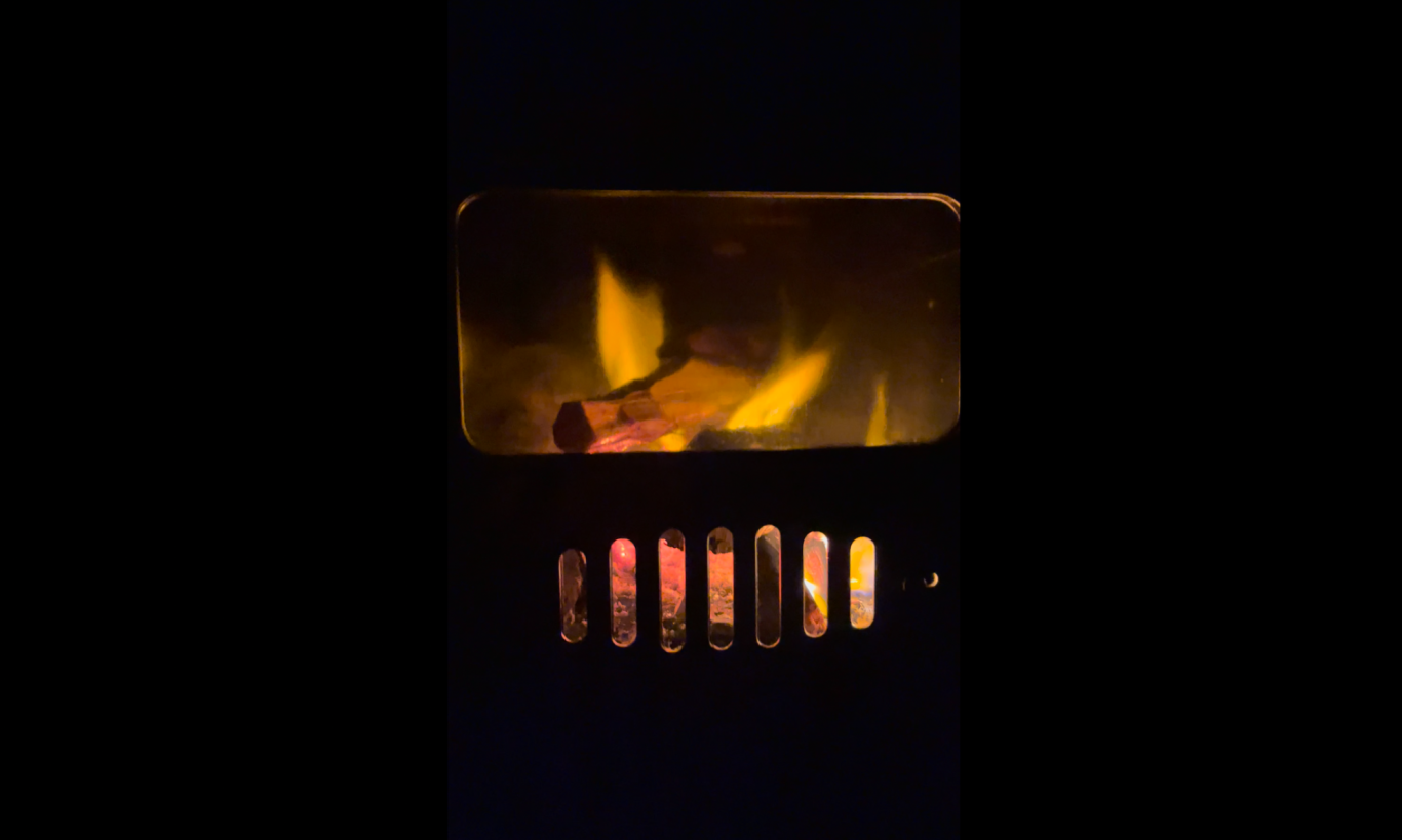 Kaminen brinner Eld flammar i en vedspis, med glödande ved och synliga grillgaller.