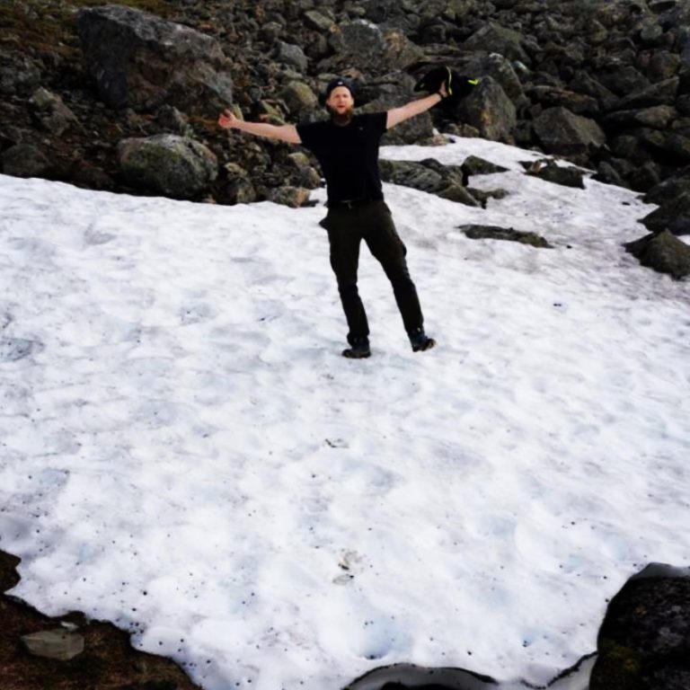 Person står med utsträckta armar på snöig mark omgiven av stenar.