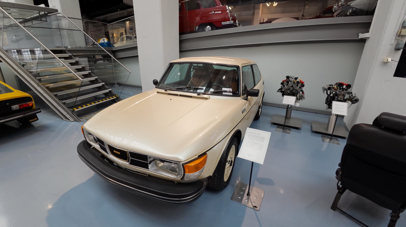 Saab Turbo En vit Saab bil stående i ett museum med motorer i bakgrunden.