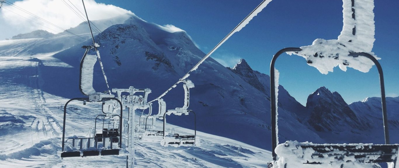 Stolslift på snötäckt alpberg med klippor i bakgrunden och klarblå himmel.