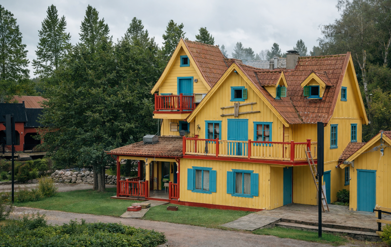 Färgglad gul och blå stuga med balkonger omgiven av träd och grönska.