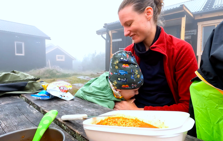 Kvinna sitter vid ett bord med ett barn som lutar sig mot henne, maträtt framför dem.